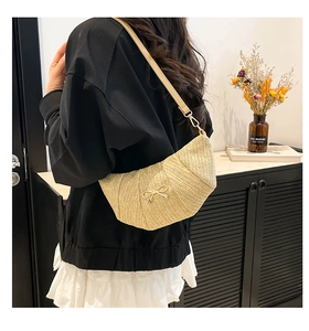 Detail of beige woven dumpling bag featuring a delicate gold bow and leather strap