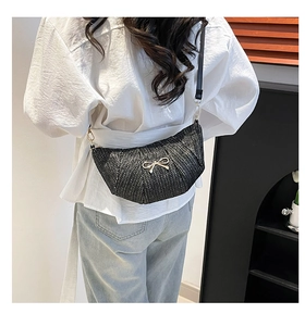 Model view of black woven crescent bag with gold bow accent and leather strap