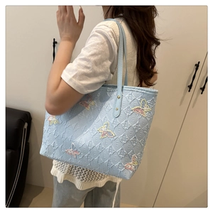 Detail view of a light blue tote bag featuring butterfly embroidery and letter patterns