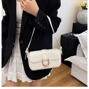Detail of white glossy baguette bag with golden horseshoe buckle and adjustable strap
