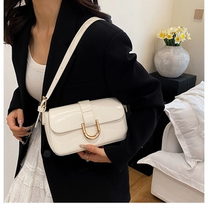 Detail of elegant beige patent leather handbag with gold U-shaped buckle on a model