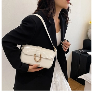 Detail of a beige patent leather underarm bag with a gold horseshoe buckle and strap