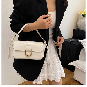 Detail of creamy white patent leather handbag with gold horseshoe buckle on model attire