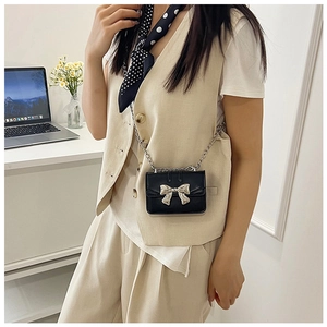 Detail of a mini black crossbody bag with a metallic silver bow and chain strap