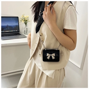Close-up of mini black crossbody bag with silver bow accent and metal chain strap