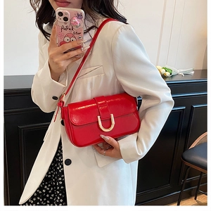 Detail of red glossy leather shoulder bag with gold metal clasp on a white suit outfit