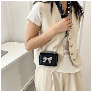 Detail of mini black crossbody bag with silver bow accent and chain strap on model