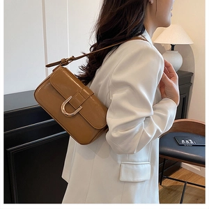 Detail of caramel brown baguette bag with golden U-buckle worn over white blazer