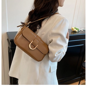 Caramel brown patent leather baguette bag with gold buckle on a model in white blazer