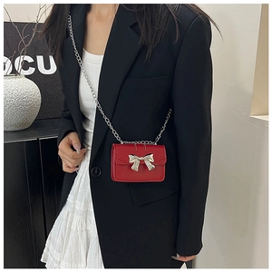 Close-up of red mini crossbody bag with silver bow accent and chain strap worn by girl