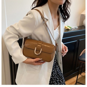 Close-up of a glossy brown shoulder bag featuring a unique golden U-shaped buckle detail