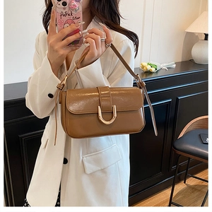 Detail of brown baguette bag with golden buckle shown on shoulder in stylish interior
