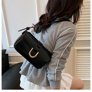 Detail of glossy black shoulder bag featuring a large gold U-shaped metal buckle and flap