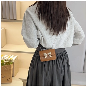 Close-up of mini brown leather crossbody bag with silver bow accent and fine chain strap