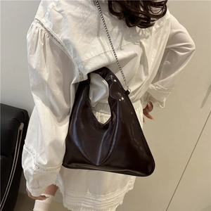 Dark brown high-gloss geometric bucket bag with silver chain strap shown on model