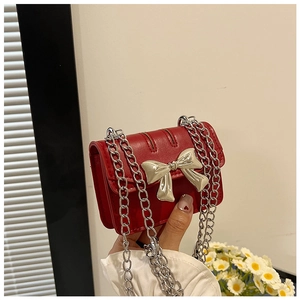 Close-up of red mini flap bag featuring a shiny silver bow clasp and chain strap