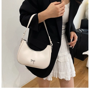 Detail of cream hobo bag with metal bow accent worn by model in black blazer