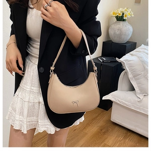 Detail of a beige crescent underarm bag with a metal bow accent and smooth matte leather