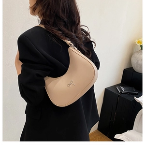 Detail of beige crescent hobo bag with silver bow accent on model's shoulder