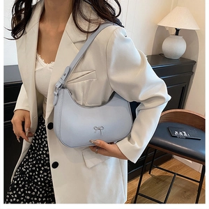 Detail of light blue crescent hobo bag with silver bow buckle on model in white suit