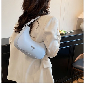 Chic light blue hobo bag with silver bow detail shown on shoulder with white blazer