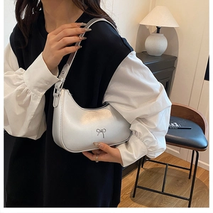 Silver crescent underarm bag featuring a metallic bow detail worn by a model