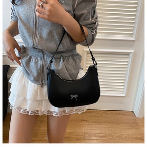 Detail of a black crescent shoulder bag with silver metal bow and adjustable strap