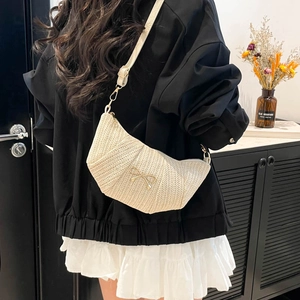 Beige woven crescent crossbody bag with golden bow ornament on a shoulder-back model