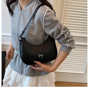 Fashionable black hobo bag with silver bow accent worn by model in casual outfit