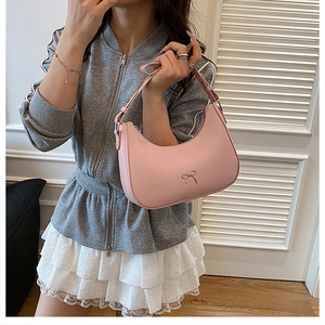 Detail of pink crescent bag showing leather texture and delicate metal bow buckle