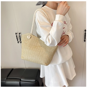 Detail of woven straw tote bag featuring thick white cotton rope handles and knot accents