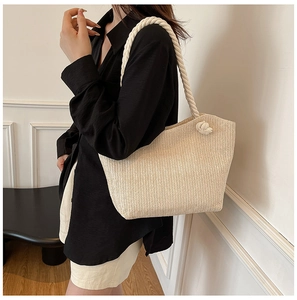 Detail of beige straw tote bag with white cotton rope handle and braided ball accent