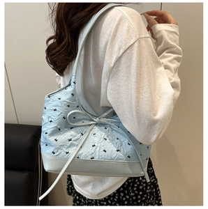 Détail du sac sous l'aisselle bleu clair avec broderie florale et nœud sur mannequin