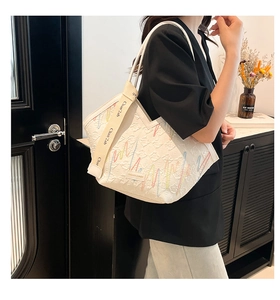 Close-up of white tote bag with colorful embroidery and branded woven shoulder strap