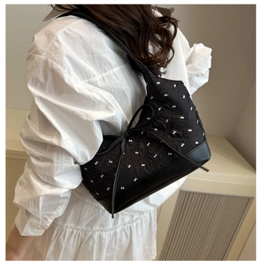 Détail d'un sac à bandoulière noir matelassé avec motifs nœuds blancs porté par un mannequin