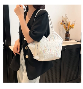 Detail of white quilted tote bag with colorful embroidery and woven ribbon handle strap