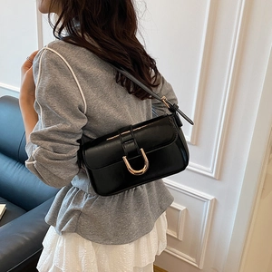 Minimalist black glossy shoulder bag with a gold horseshoe buckle on a female model