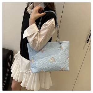 Detail of light blue bubble textured tote bag with colorful embroidered butterfly patterns