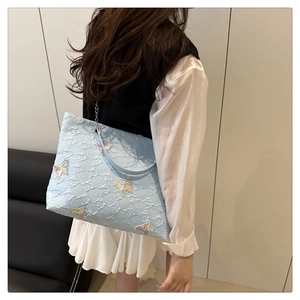 Close-up of light blue tote bag featuring colorful sequined butterfly embroidery and chain strap