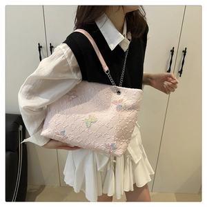 Detailed texture of pink tote bag with colorful butterfly embroidery and metal chain strap