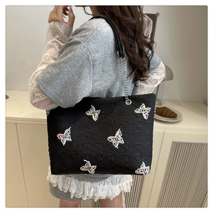 Detail of black tote bag featuring colorful butterfly embroidery and metal chain strap
