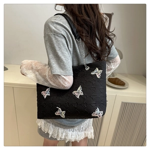 Woman wearing large black floral embroidered tote bag with chain strap in casual setting