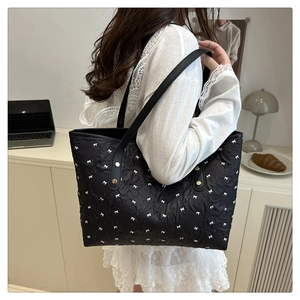Borsa tote trapuntata nera con stampa a fiocchi bianchi e rivetti dorati portata da una modella