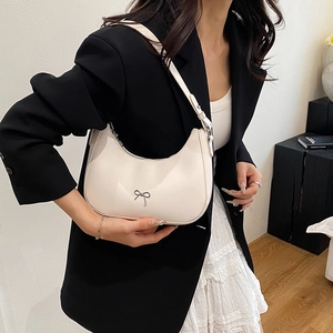 Creamy white moon-shaped shoulder bag with silver bow accent worn by a model