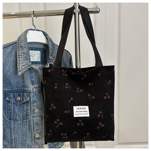 Detail of red cherry embroidery and fashion label on black corduroy tote bag surface