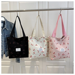 Detailed view of three corduroy tote bags with cherry patterns in black, beige and pink