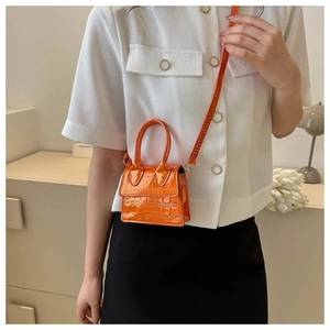 Detail showing bright orange crocodile embossed texture and mini dual handles on the bag