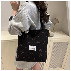 Detail of black corduroy tote bag featuring red cherry embroidery and fashion label