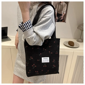 Detailed view of black corduroy tote bag with red cherry prints and woven handle