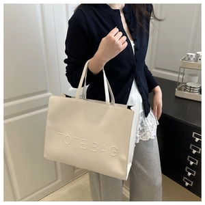 Detail of cream white faux leather tote bag with embossed letters held by a model